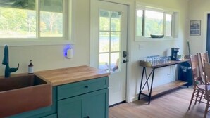 A kitchen with teal cabinets, a wooden countertop, and a window overlooking greenery. - Camp Blue Canoe - Creekside Cottage  (Three Rivers)