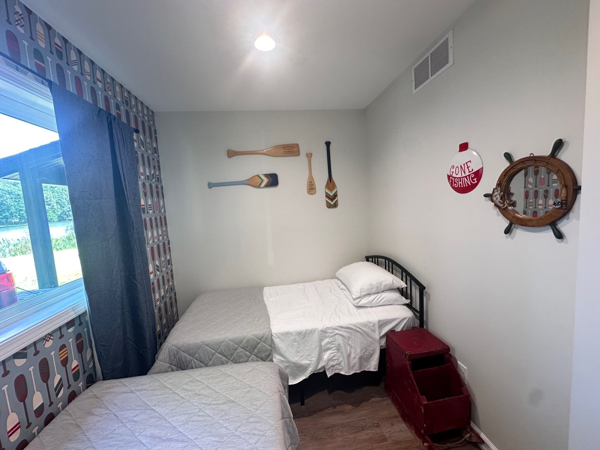 A bedroom with two beds, a window with a view, and nautical-themed decorations.