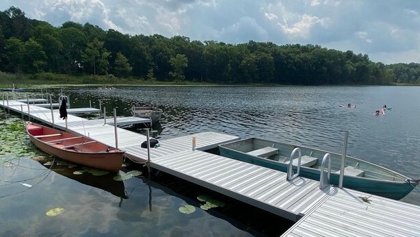 A dock with boats, a wooden pier, and a calm lake with trees in the background. - Camp Blue Canoe - Creekside Cottage  (Three Rivers)