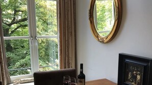 A room with a large window, a framed mirror, a table with a bottle of wine, glasses, and a framed picture. - In the Heart of Old Amsterdam with Canal view (Amsterdam)