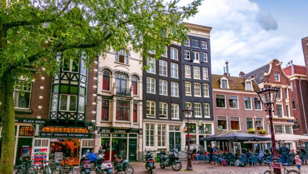 A cobblestone street lined with historic buildings, bicycles parked along the sidewalk, and outdoor seating at a café. - In the Heart of Old Amsterdam with Canal view (Amsterdam)