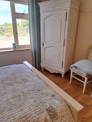 Une chambre à coucher avec un grand lit, une armoire blanche, une chaise et une fenêtre donnant sur l’extérieur.