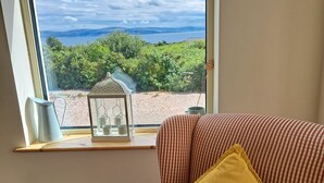 A room with a large window overlooking a scenic landscape, a cushioned bench, and a small table with a lantern.