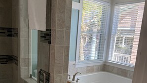 A modern bathroom with a walk-in shower, a freestanding bathtub, and a window with blinds.