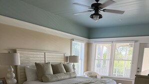 A bedroom with a bed, nightstands, a ceiling fan, and large windows.