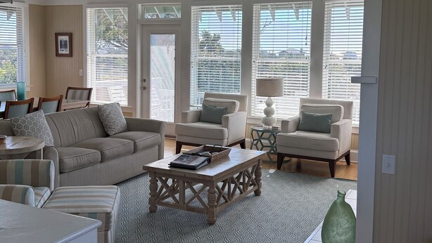 A spacious living room with a high ceiling, large windows, and a ceiling fan.