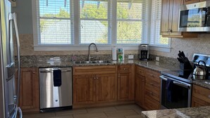 A modern kitchen with wooden cabinets, stainless steel appliances, and large windows.