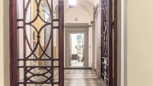 Un pasillo con suelo de cuadros, una puerta de madera con celosía decorativa y vista a una habitación con una silla y una mesa.