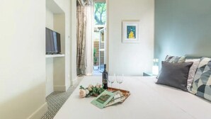 Habitación de hotel con cama, televisor, un cuadro en la pared y una bandeja con una botella y vasos en el suelo.