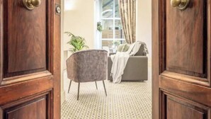 Una habitación con suelo estampado, un sillón gris, un sofá y una ventana con cortinas.