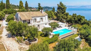 Eine moderne Villa mit Schwimmbad, umgeben von üppiger Vegetation und mit Blick auf ein Gewässer.