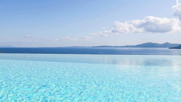 Ein klares, blaues Schwimmbecken mit Blick auf das Meer und ferne Berge.