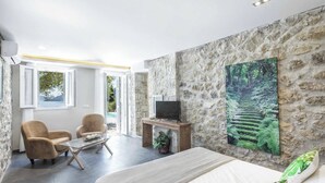 Ein modernes Schlafzimmer mit Steinwand, einem Bett, einem Fernseher auf einem Holzboden und einem Waldgemälde.