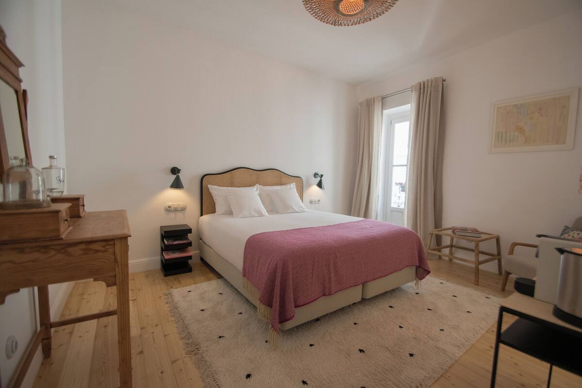 A bedroom with a bed, bedside lamps, a wooden desk, a small table, and a chair.