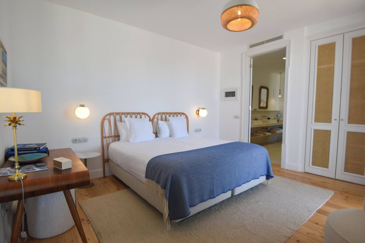 A bedroom with a bed, bedside table, lamp, and a view of a bathroom.