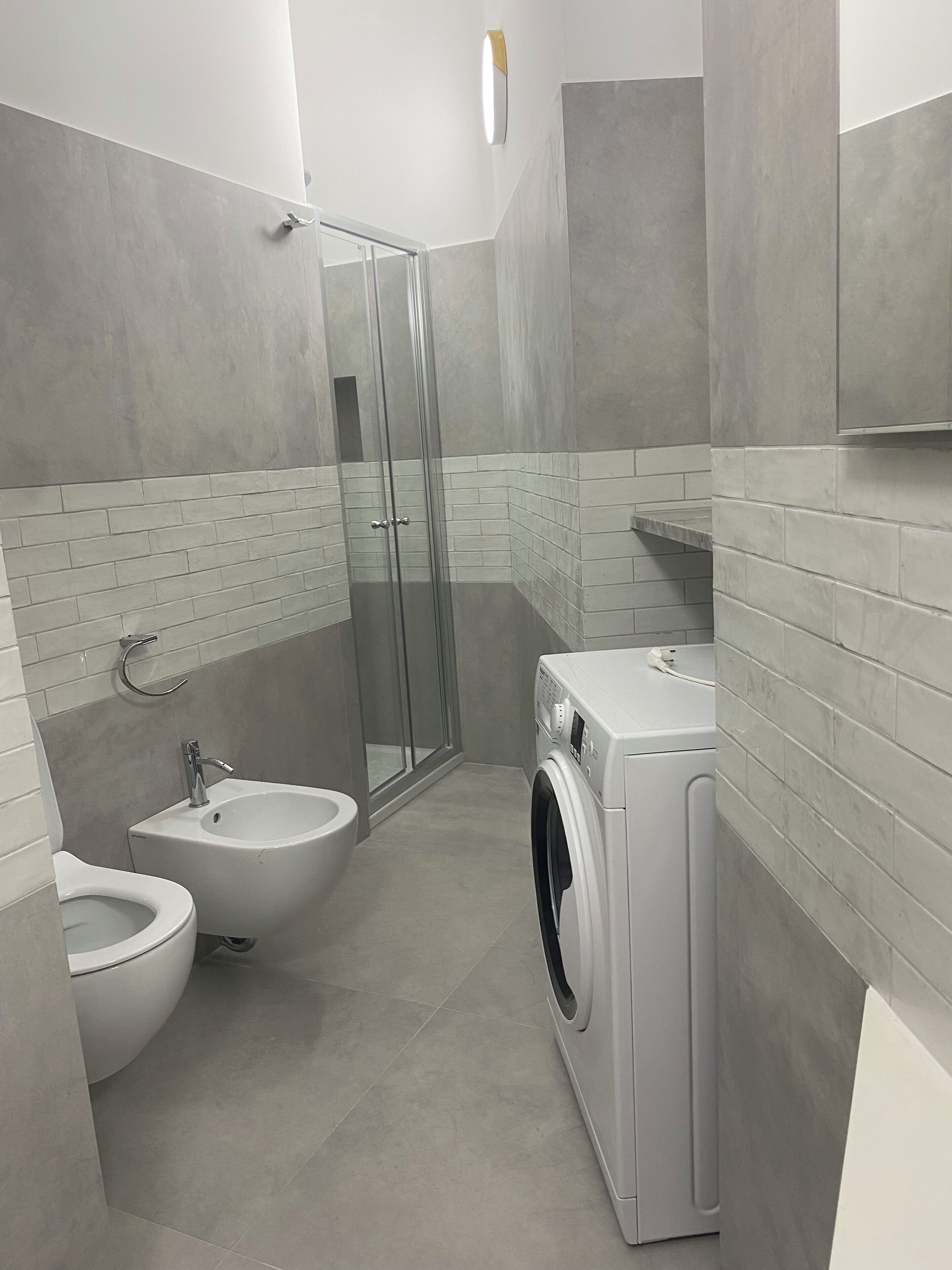 Un bagno moderno con box doccia in vetro, un bidet, una lavatrice e un water.