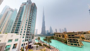 A high-rise building with a modern design, a river with palm trees, and a prominent skyscraper in the background. - Amazing 1 Bed l Burj Khalifa Views l King Size Bed (Downtown Dubai)