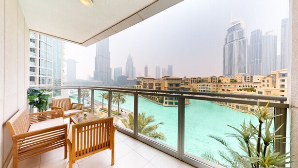 A balcony with wooden furniture overlooking a cityscape and a turquoise body of water. - Amazing 1 Bed l Burj Khalifa Views l King Size Bed (Downtown Dubai)