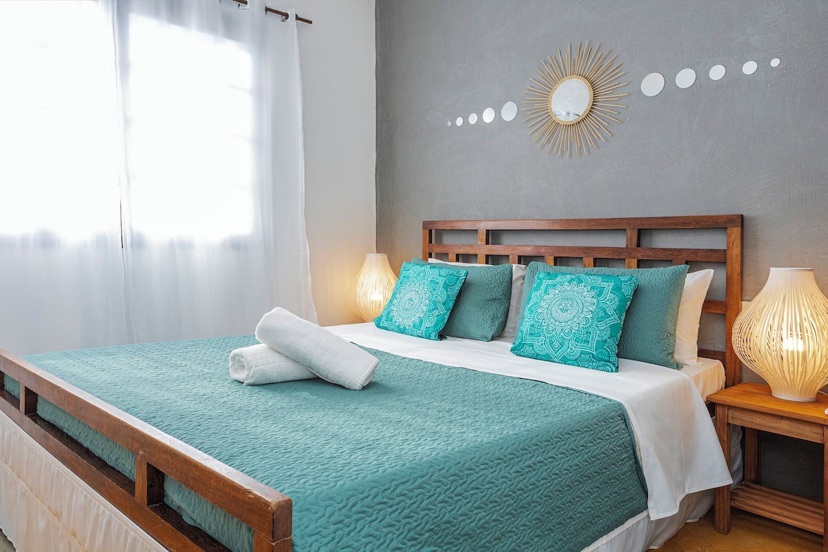 A neatly made bed with a teal bedspread and white linens, a wooden headboard, and two bedside lamps.