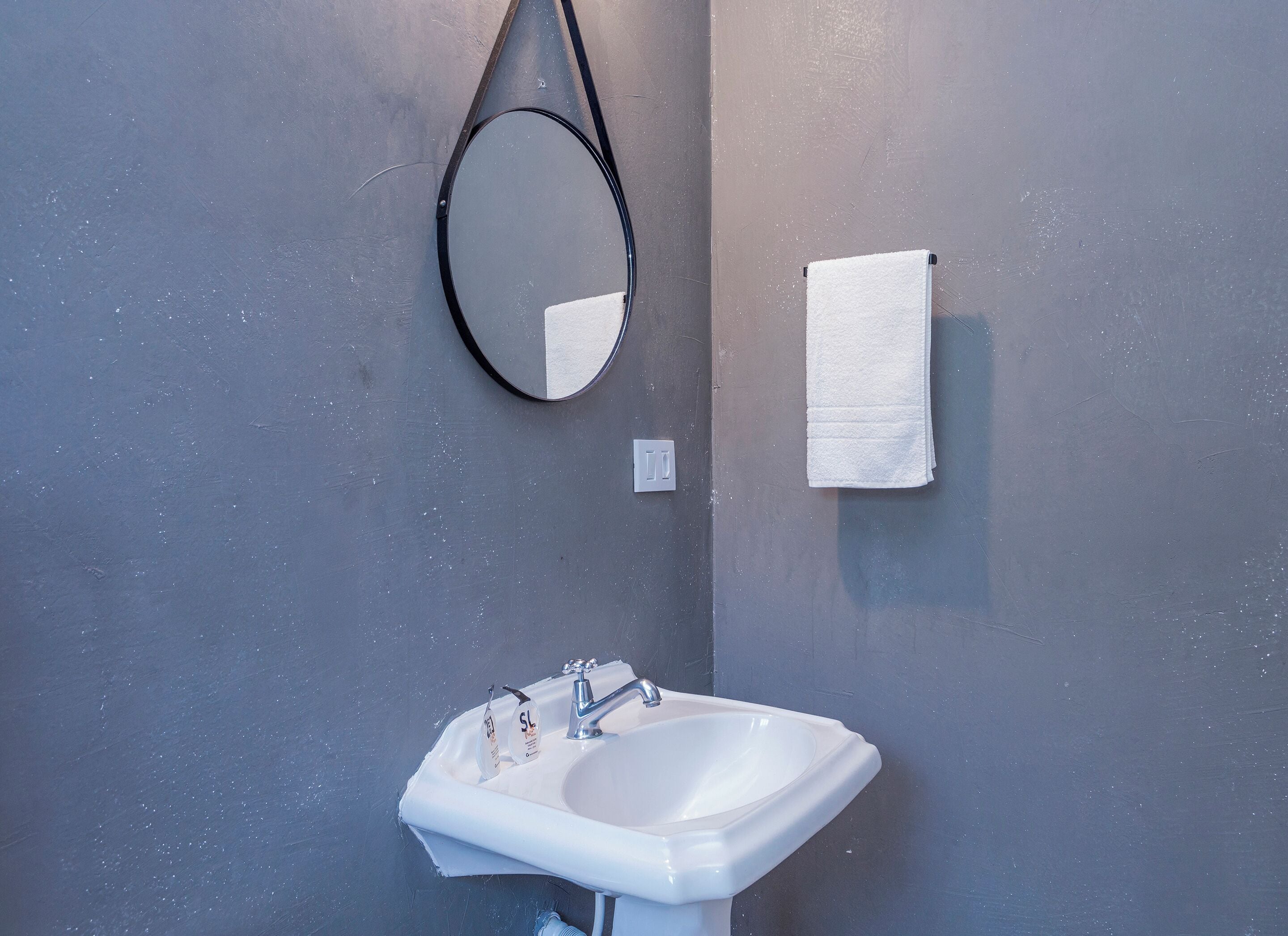 A bathroom with a white sink, a mirror, and a towel hanging on the wall.