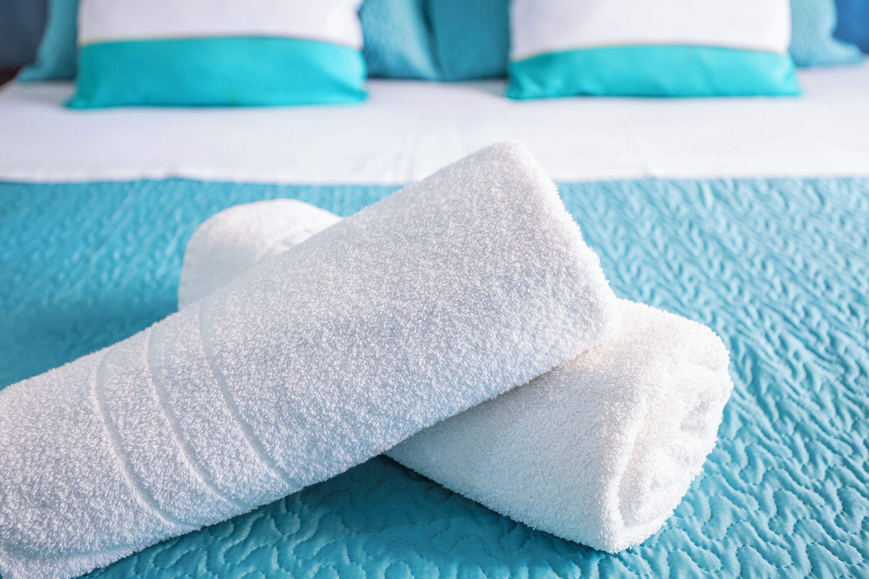 A bed with a blue quilt and white pillows with teal accents.