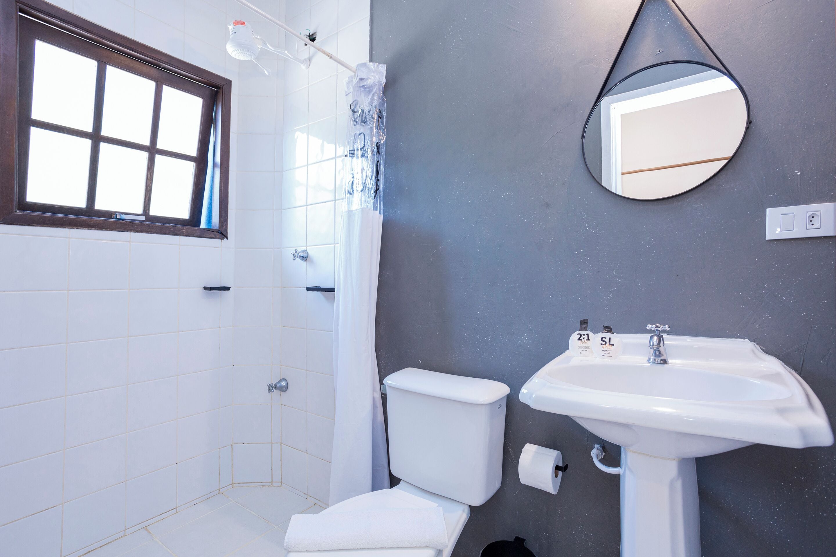 Un baño con inodoro blanco, lavamanos, espejo y ventana.