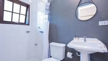Un baño con inodoro blanco, lavamanos, espejo y ventana.