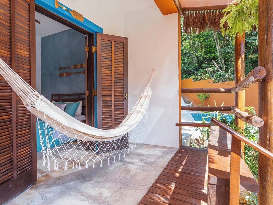 A hammock on a wooden deck with a view of a pool and lush greenery.