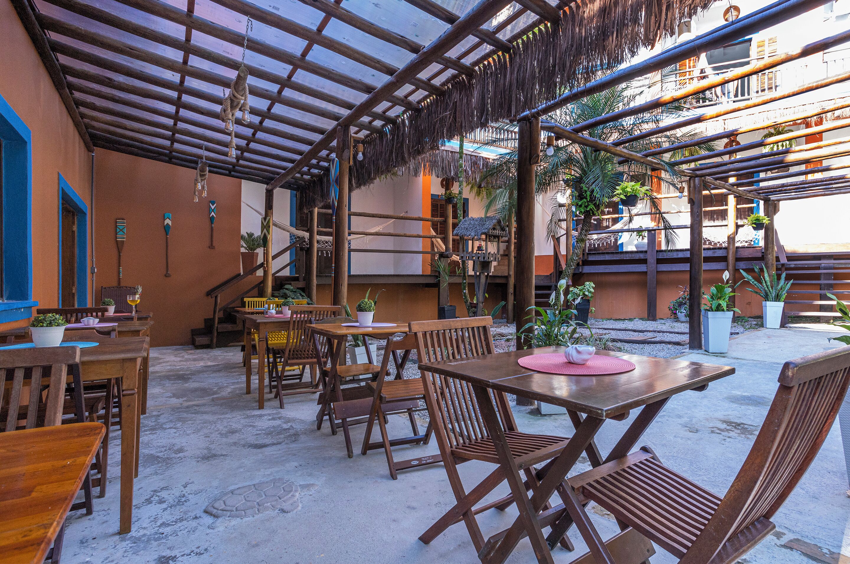 Une terrasse extérieure avec des tables et des chaises en bois, un toit de chaume et des plantes en pot.