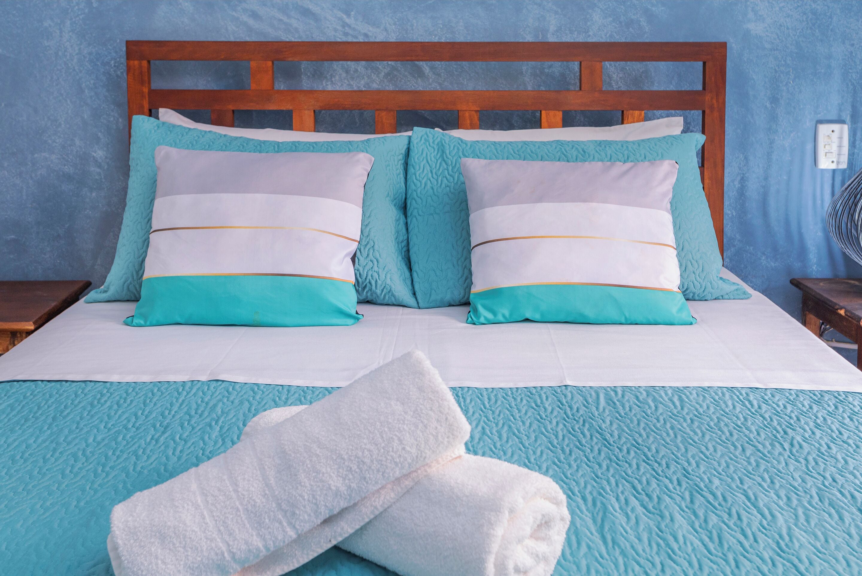 A neatly made bed with a blue and white bedspread, two matching pillows, and a folded white towel on the bed.