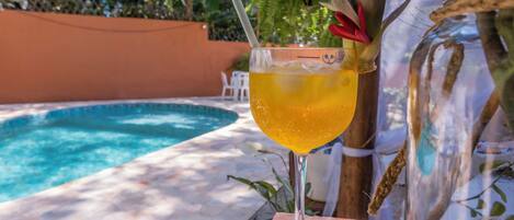 A glass of yellow drink with a straw and a decorative flower, placed on a wooden table by a pool.