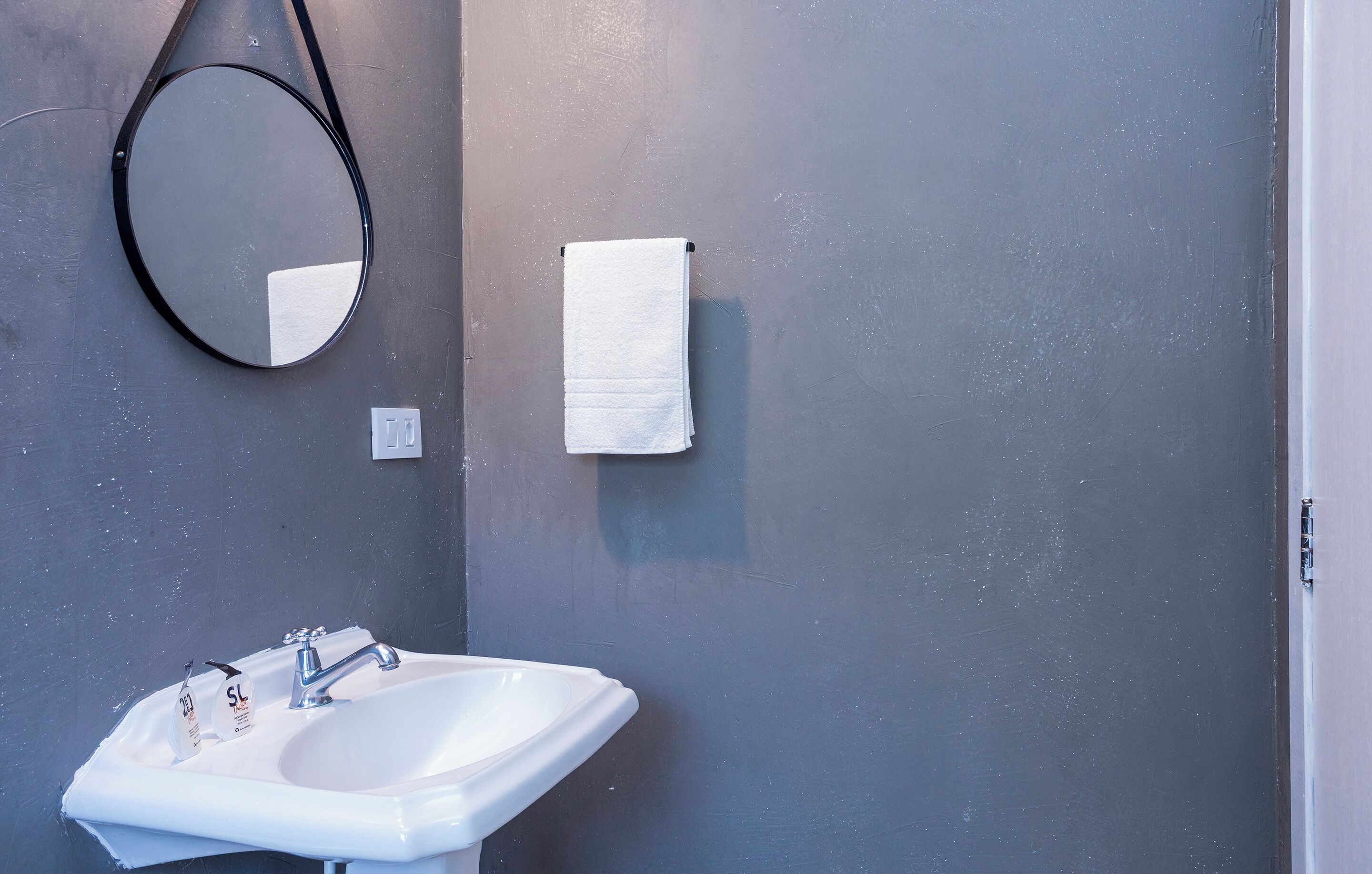 A bathroom with a white sink, a round mirror, and a white towel hanging on the wall.
