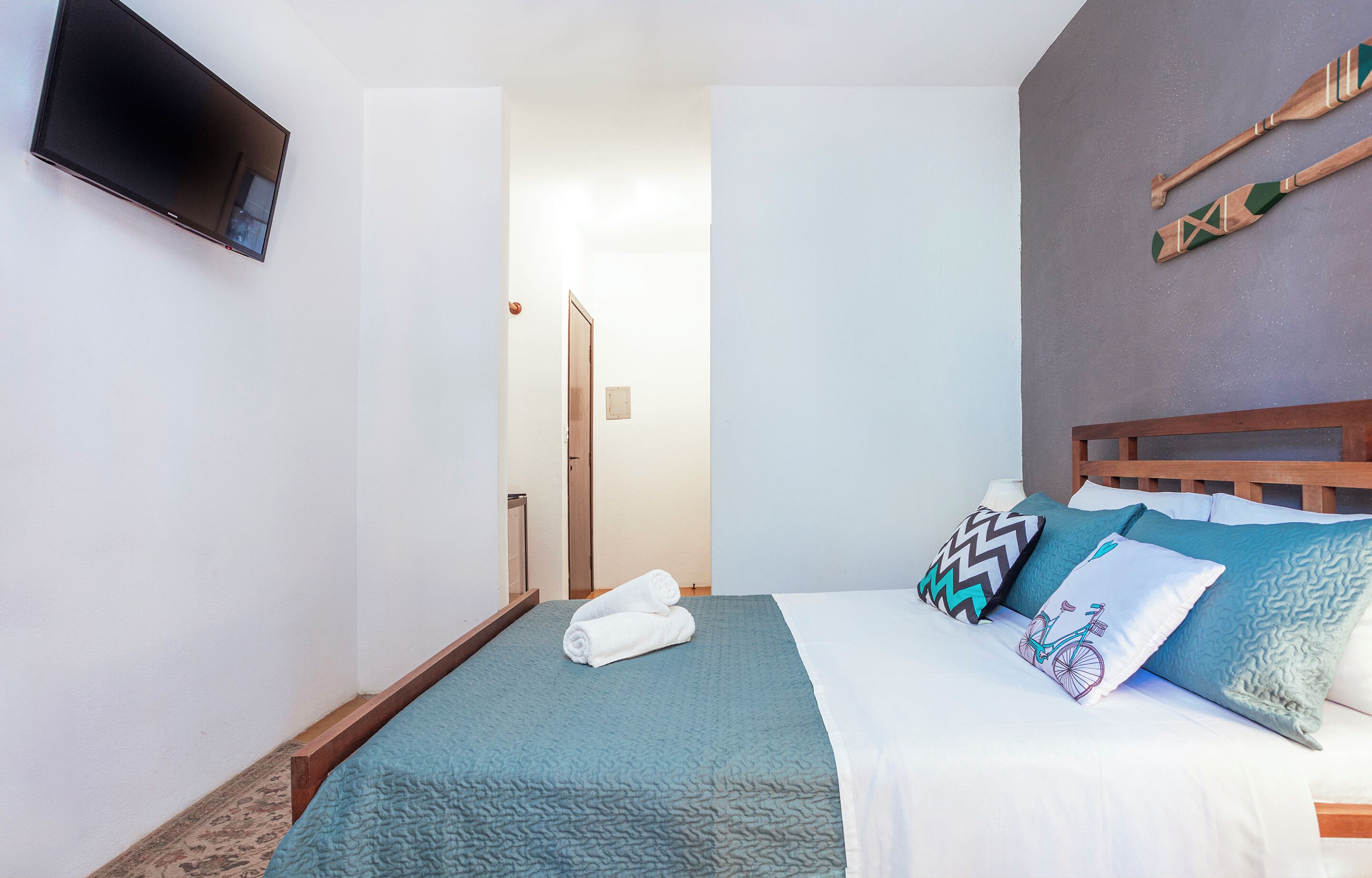 A hotel room with a bed, a flat-screen TV mounted on the wall, and a wooden headboard.