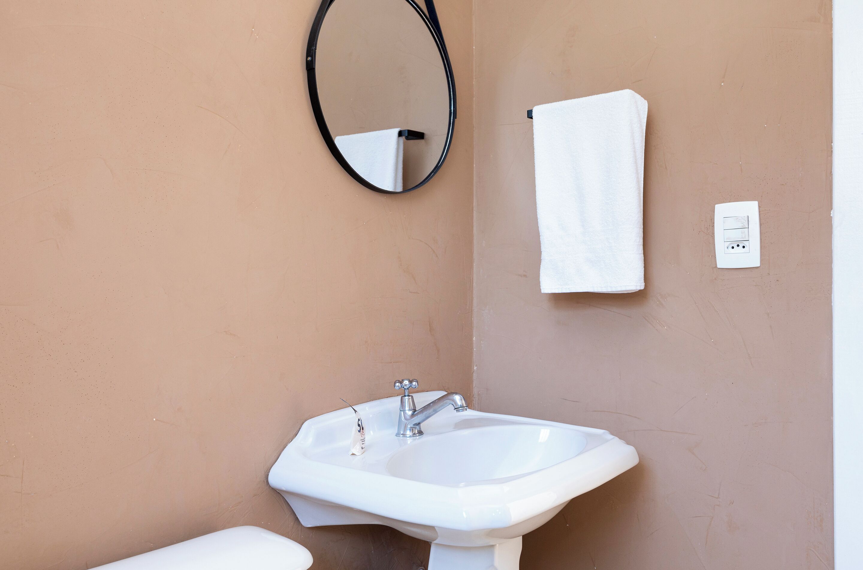 Un baño con un lavamanos blanco, un espejo y una toalla colgada en la pared.