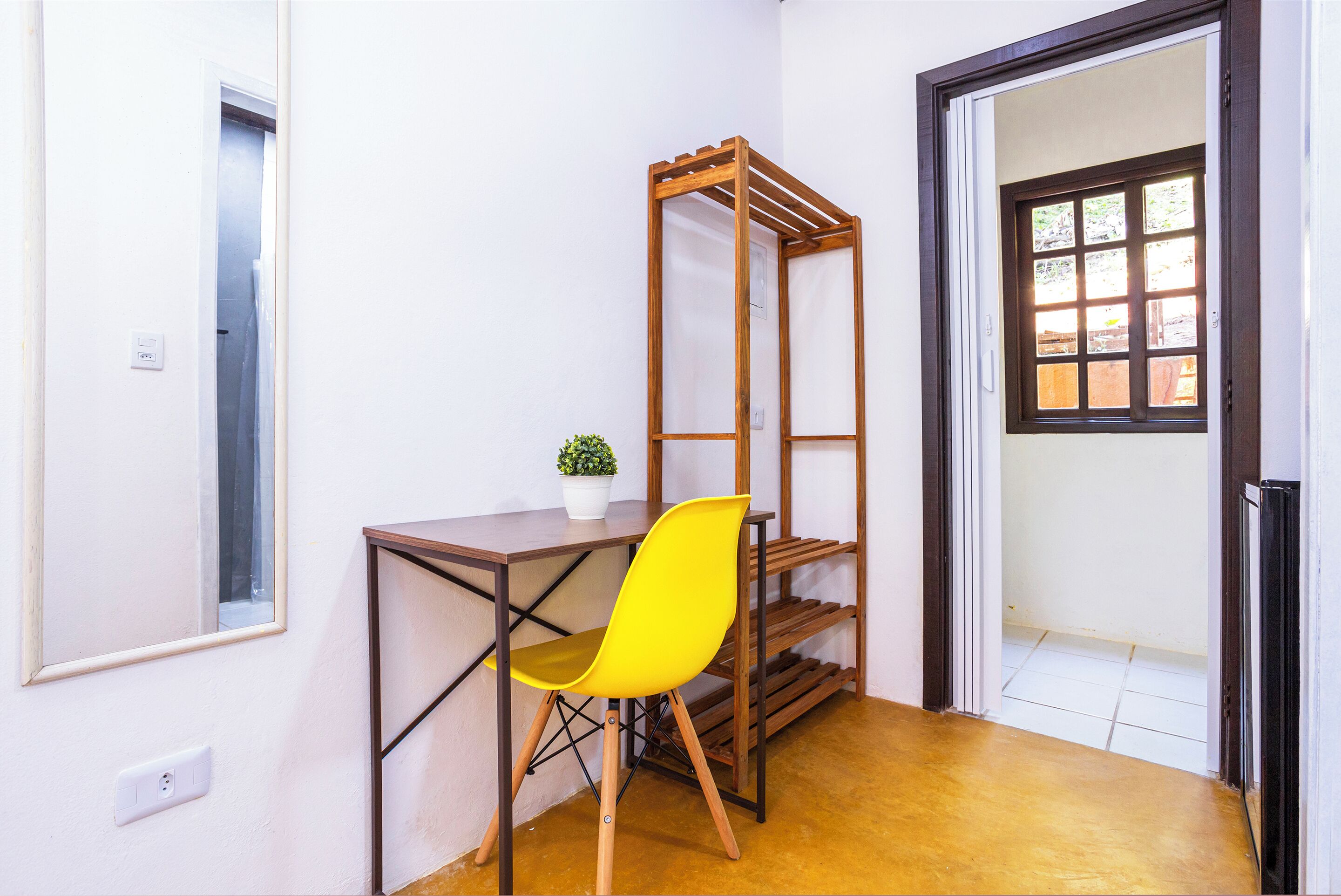 A small room with a wooden desk, a yellow chair, a small potted plant, and a wooden shelving unit.
