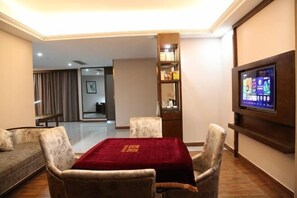 A living room with a TV, a sofa, a dining table with chairs, a bookshelf, and a staircase leading to another room. - Jianan Business Hotel (Yongzhou)