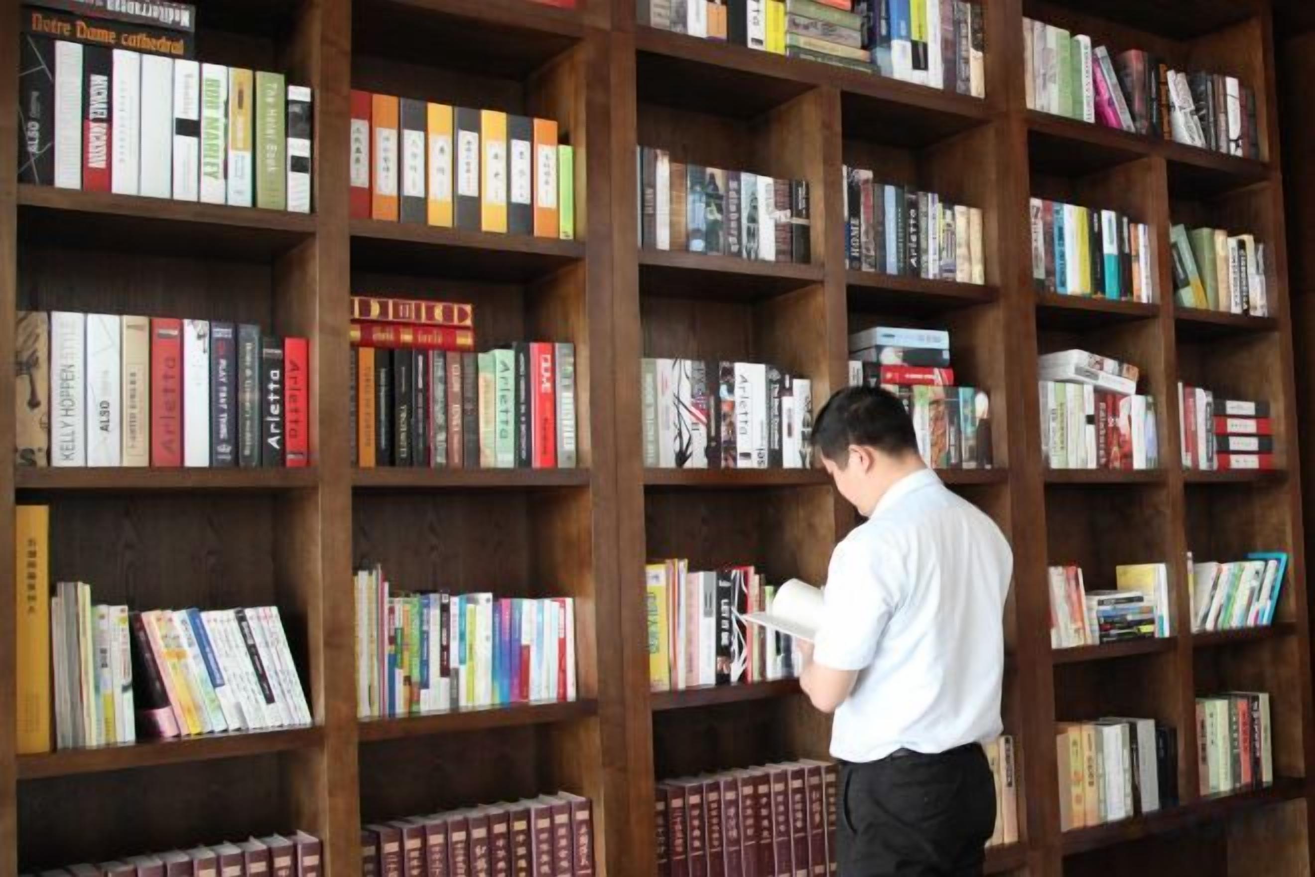 A person browsing books in a library with multiple wooden bookshelves.