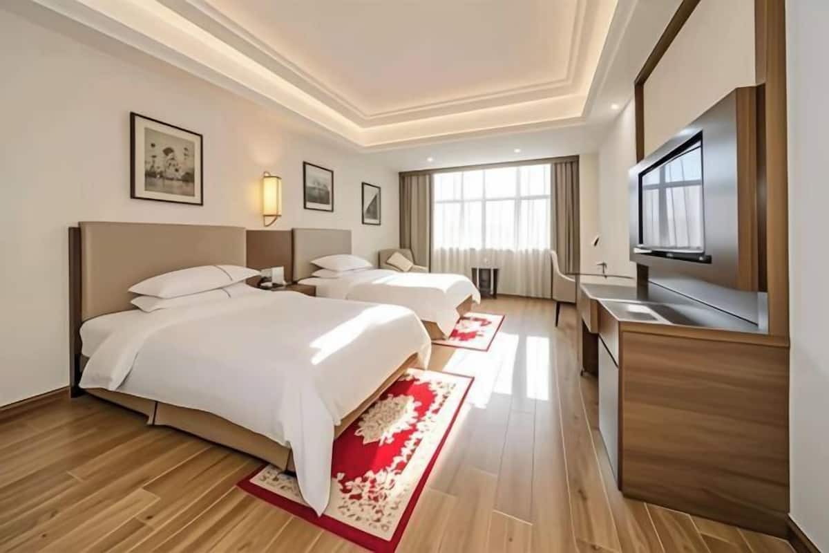 Habitación de hotel con dos camas, televisión, escritorio y un ventanal grande.