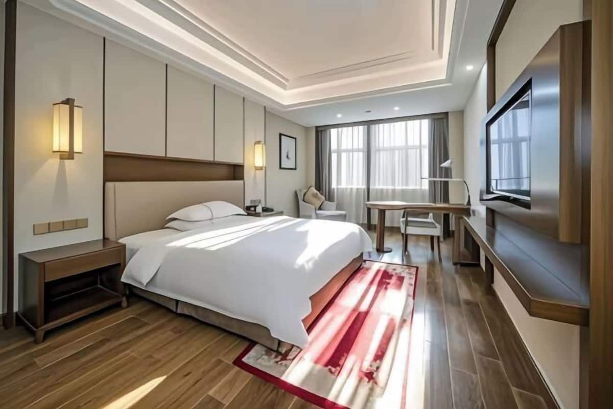 Habitación de hotel con una cama grande, mesitas de noche, un escritorio, una silla, un televisor y un ventanal.