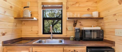 A compact kitchen with wooden walls, a sink, a microwave, a coffee maker, and a dishwasher.