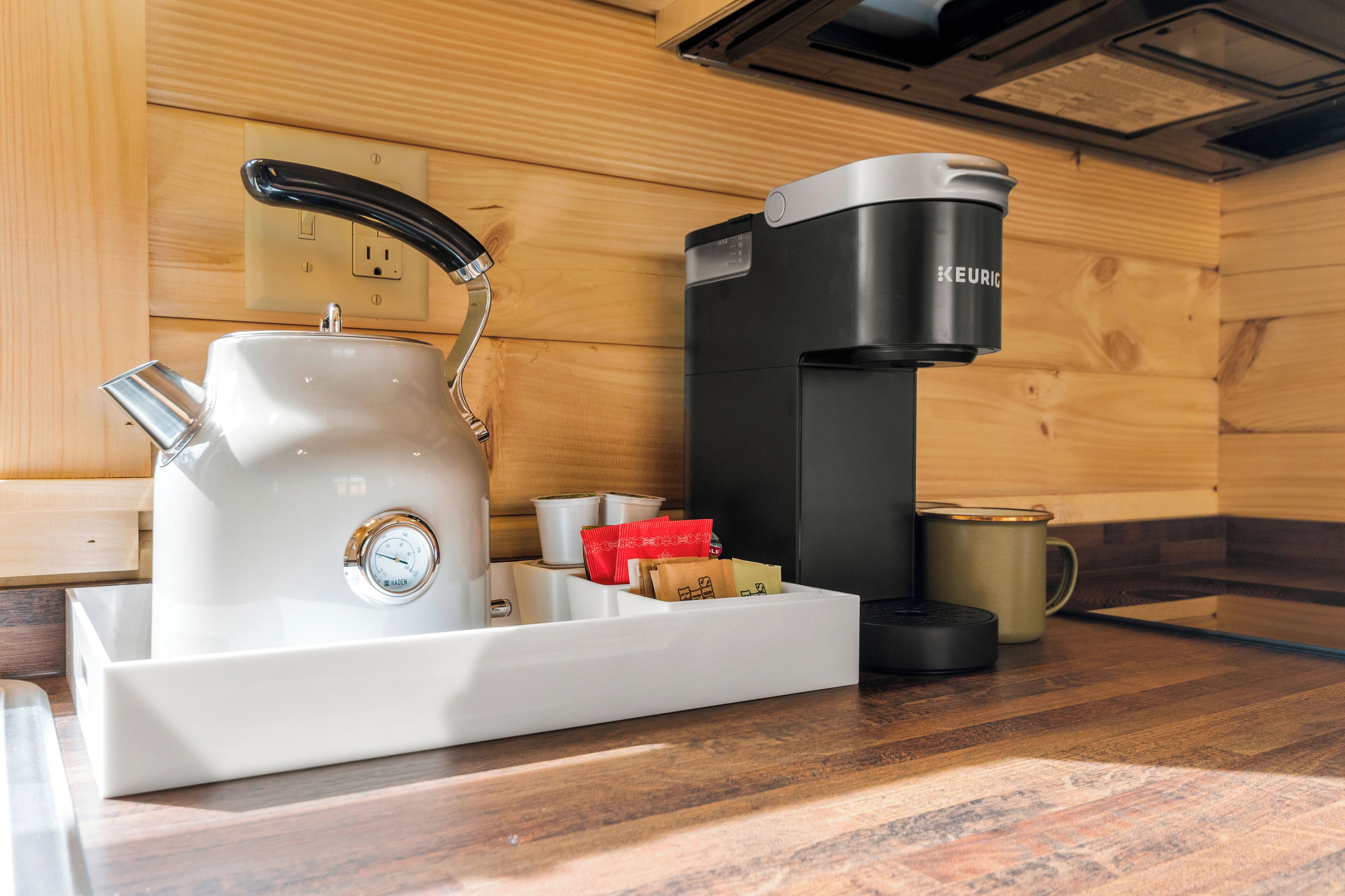 Een kitchenette met een waterkoker, koffiezetapparaat en een dienblad met theezakjes en een mok.