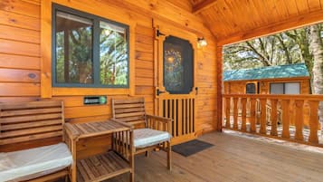 A wooden cabin with a porch, two wooden benches, a table, and a door with a decorative glass panel.