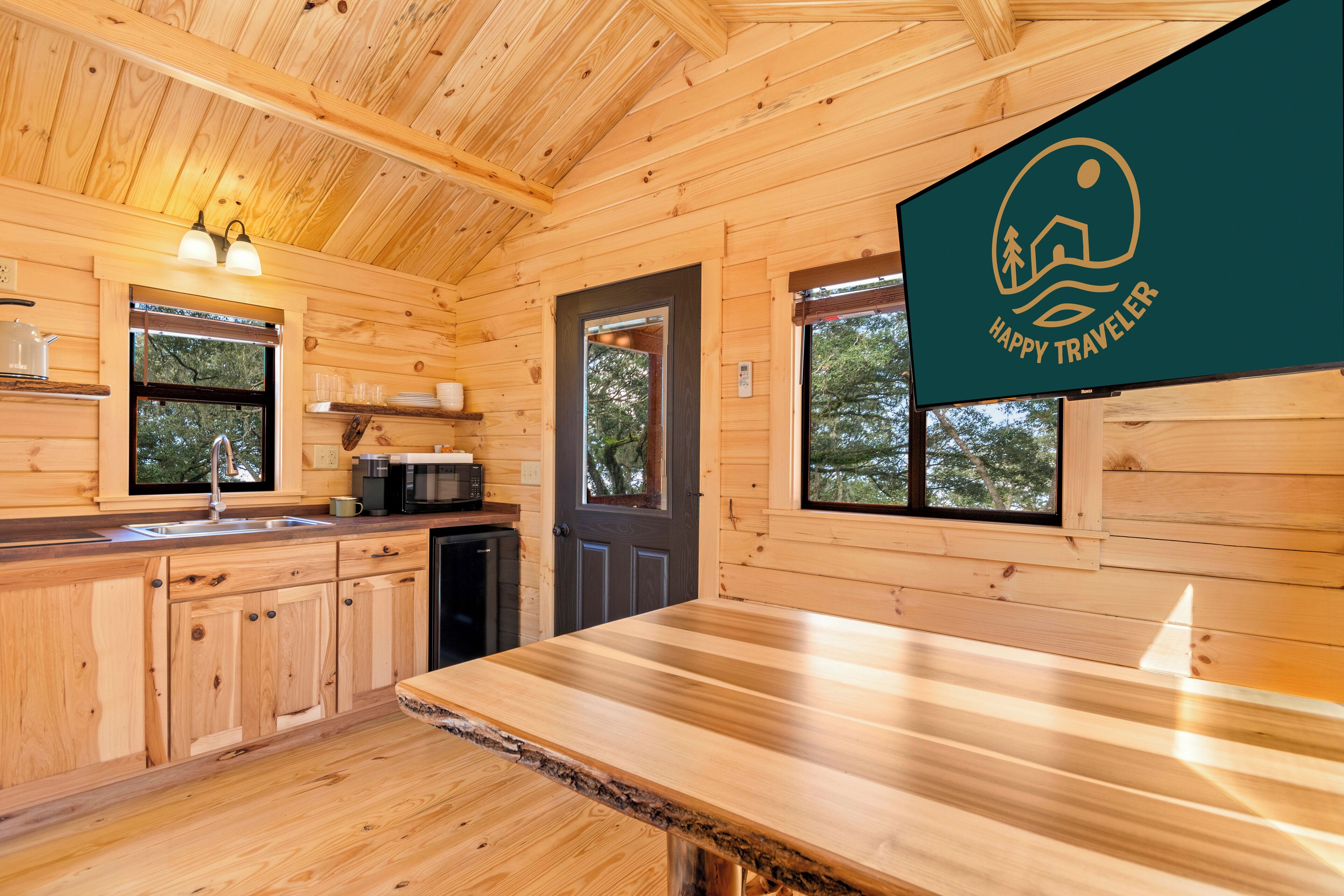 A wooden cabin interior with a kitchen area, wooden cabinets, a countertop, and a door with a window.