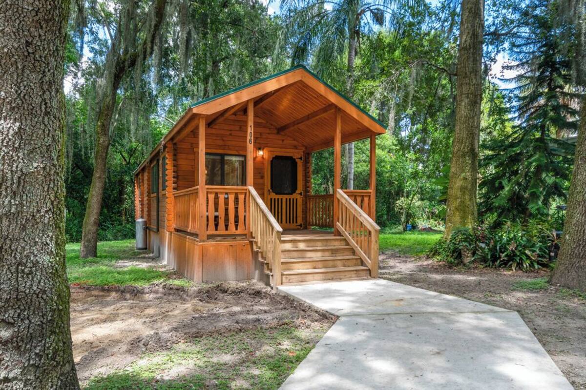 A wooden cabin with a porch and stairs, surrounded by trees.