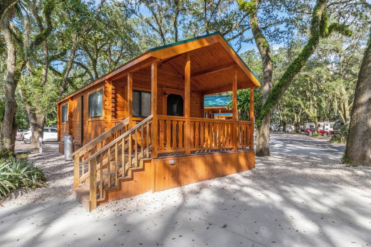 A wooden cabin with a porch and stairs, surrounded by trees.