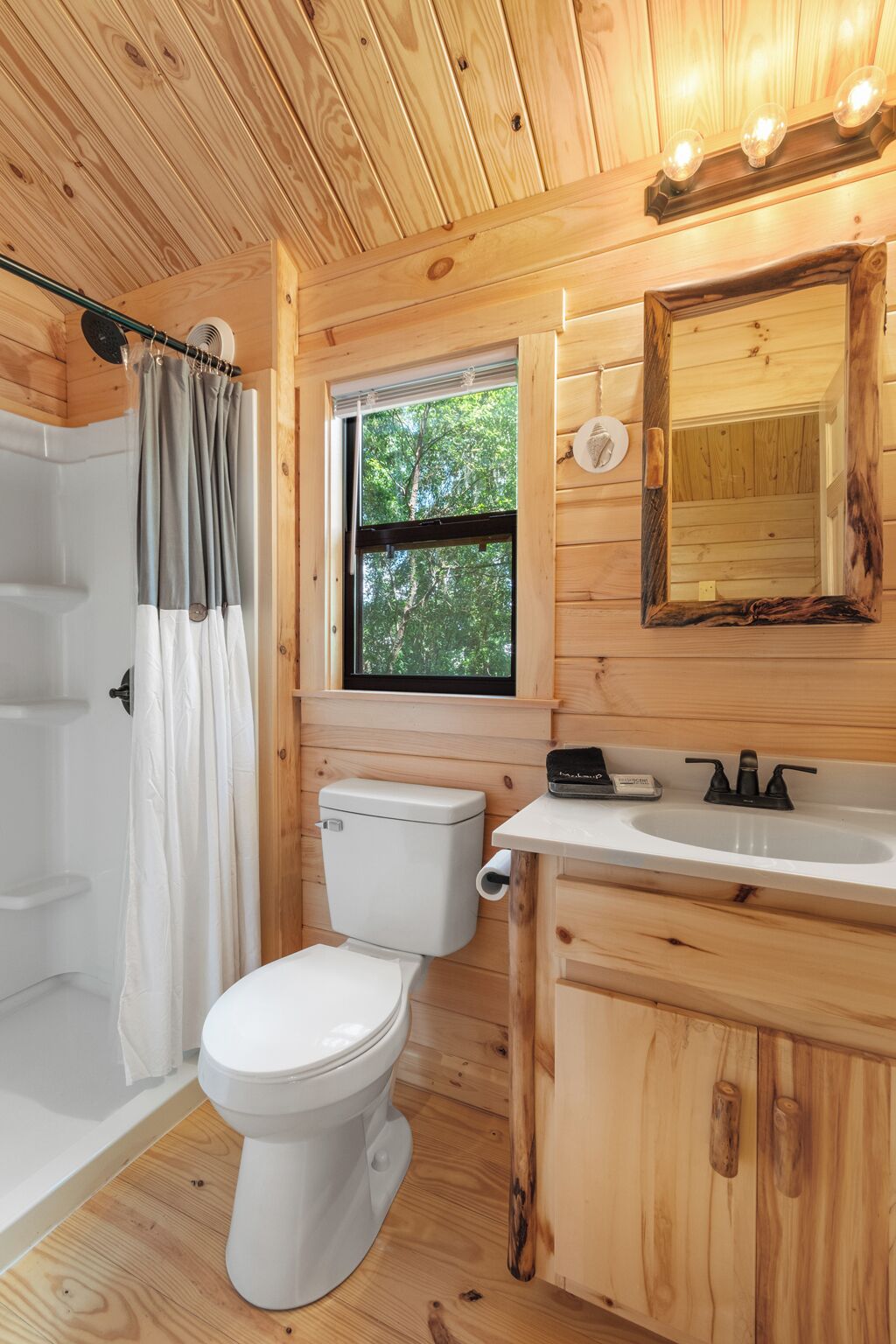 A wooden cabin bathroom with a toilet, sink, and shower.
