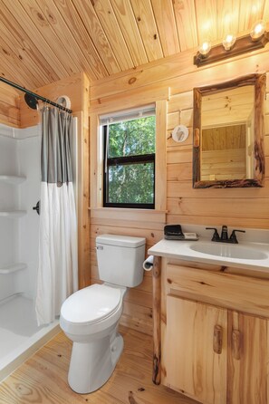 A wooden cabin bathroom with a toilet, sink, and shower. - Happy Travelers RV Resort (Thonotosassa)