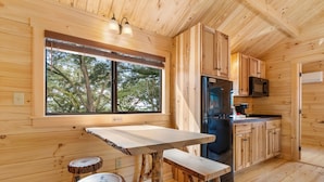 A wooden cabin interior with a kitchen area, a dining table, and two stools. - Happy Travelers RV Resort (Thonotosassa)