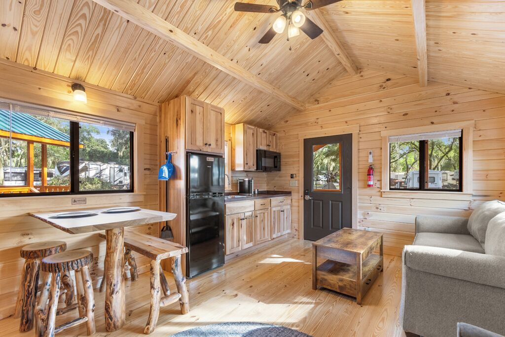A wooden cabin interior with a kitchen, dining area, and seating space.