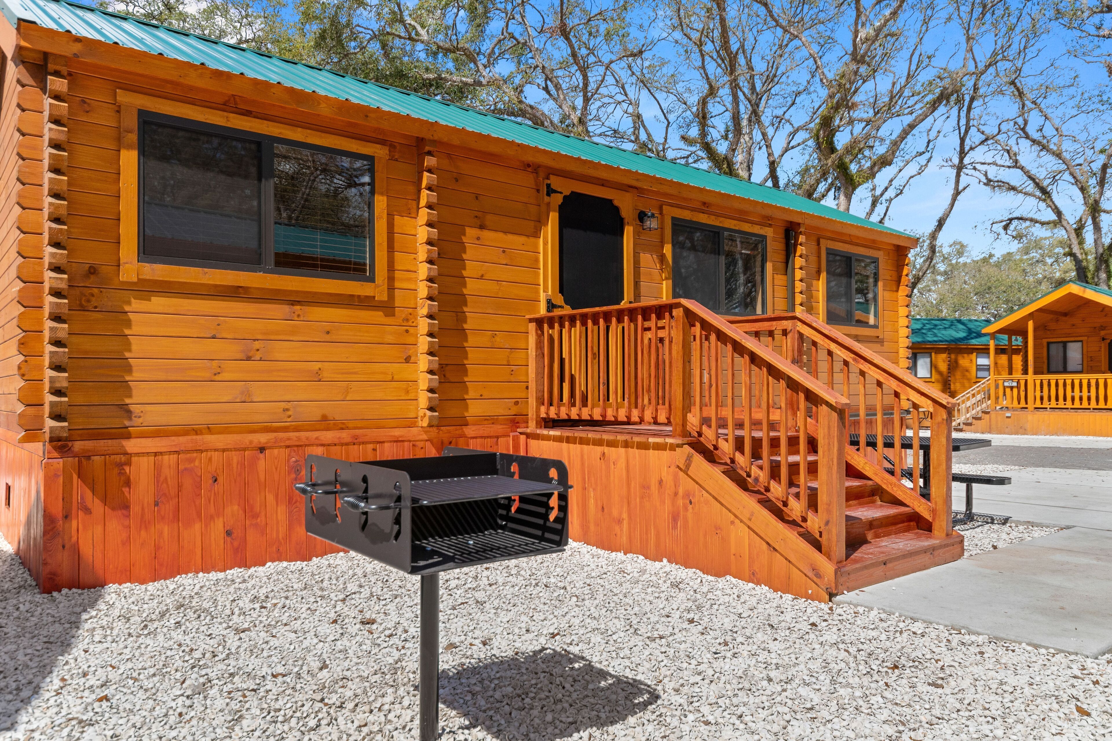 Une cabane en bois avec un toit vert, une terrasse en bois et un barbecue.